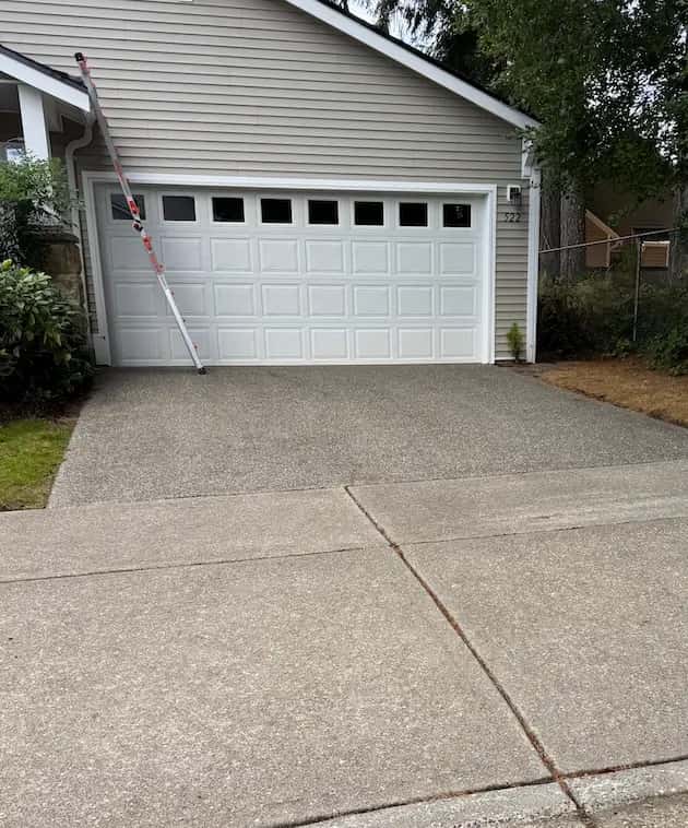 Clean exposed-aggregate driveway and concrete sidewalk in front of a white garage door after pressure washing.