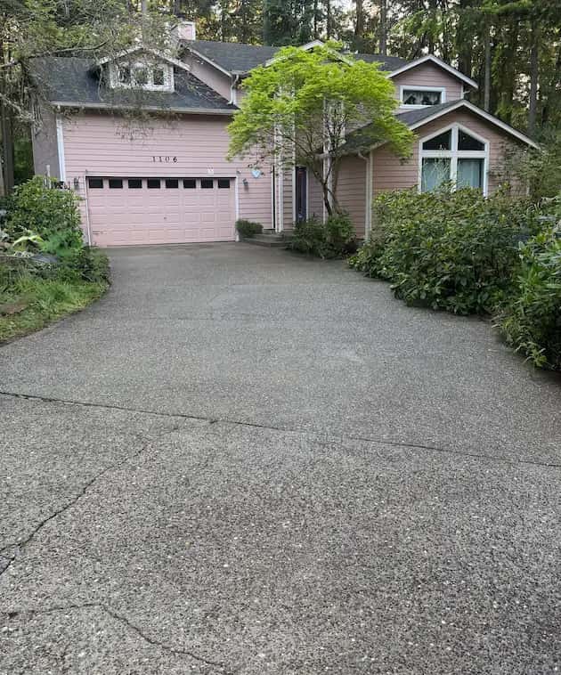 Clean exposed-aggregate driveway leading to a pink two-story home with matching pink garage door.