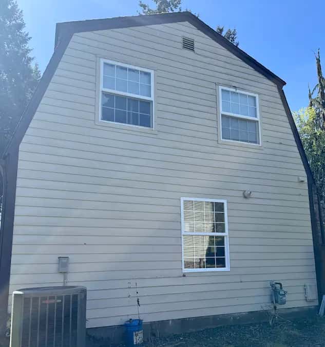 Clean beige lap siding on the gable end of a gambrel-roof house after a soft wash, blue sky behind.