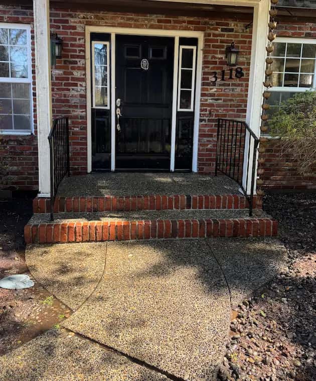 Clean red brick front steps and exposed-aggregate concrete walkway leading to a black front door.