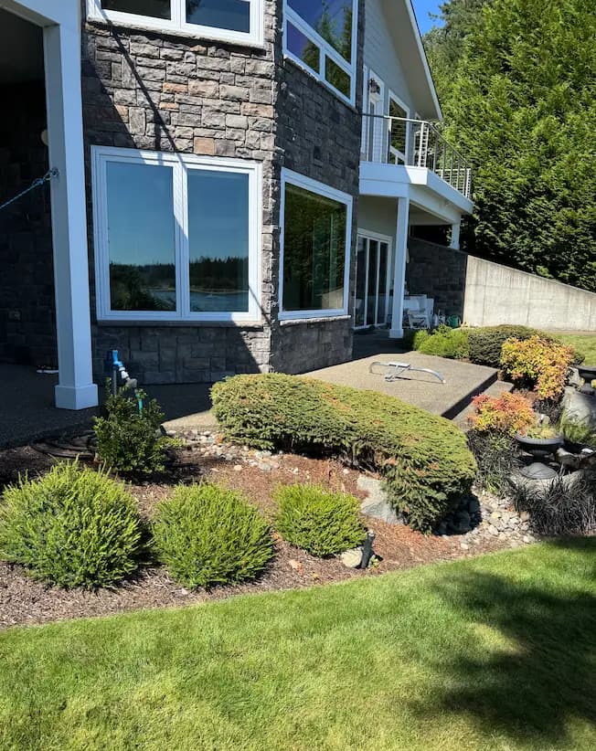 Freshly cleaned large windows on a stone-veneer home with white trim, landscaped shrubs and lawn in front.
