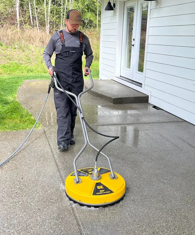 Technician in bib overalls cleaning a concrete patio with a yellow 20-inch Whirl-A-Way surface cleaner.