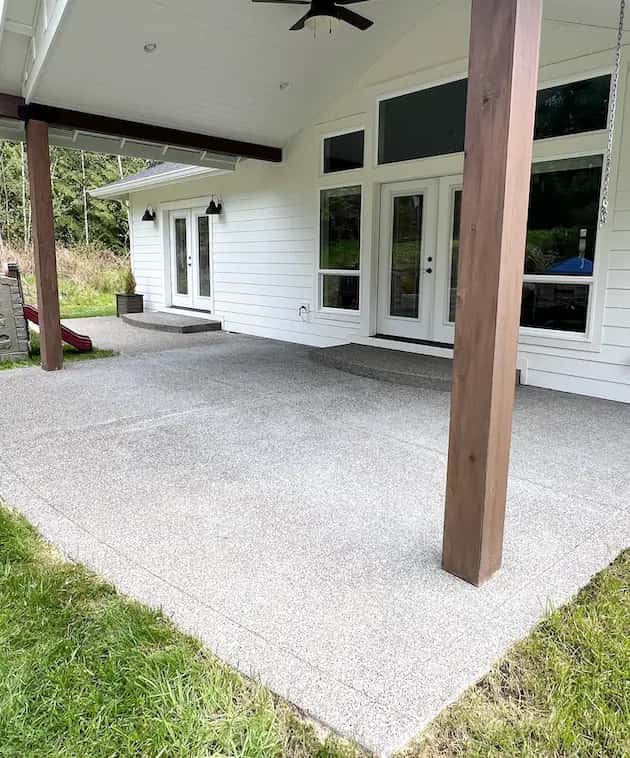 Bright, clean exposed-aggregate concrete patio under a covered porch with timber posts after pressure washing.