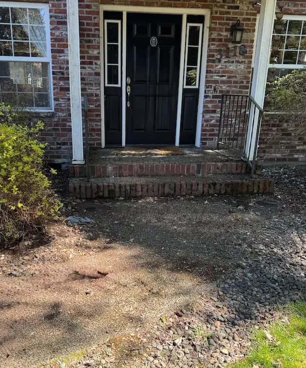 Dirty brick front steps and debris-covered concrete walkway leading to a black front door, before pressure washing.