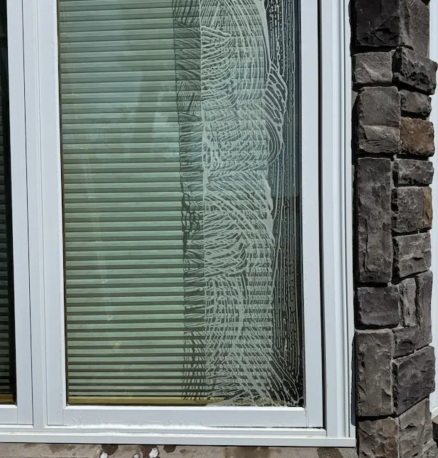 Exterior window partly covered in soapy cleaning solution swirls, white frame beside a stacked-stone wall.