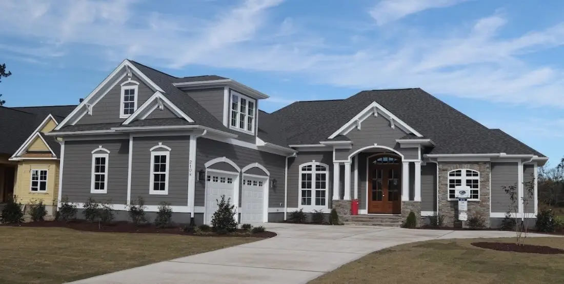Gray lap-siding craftsman-style home with white trim, stone accents, wood front door and a clean concrete driveway.