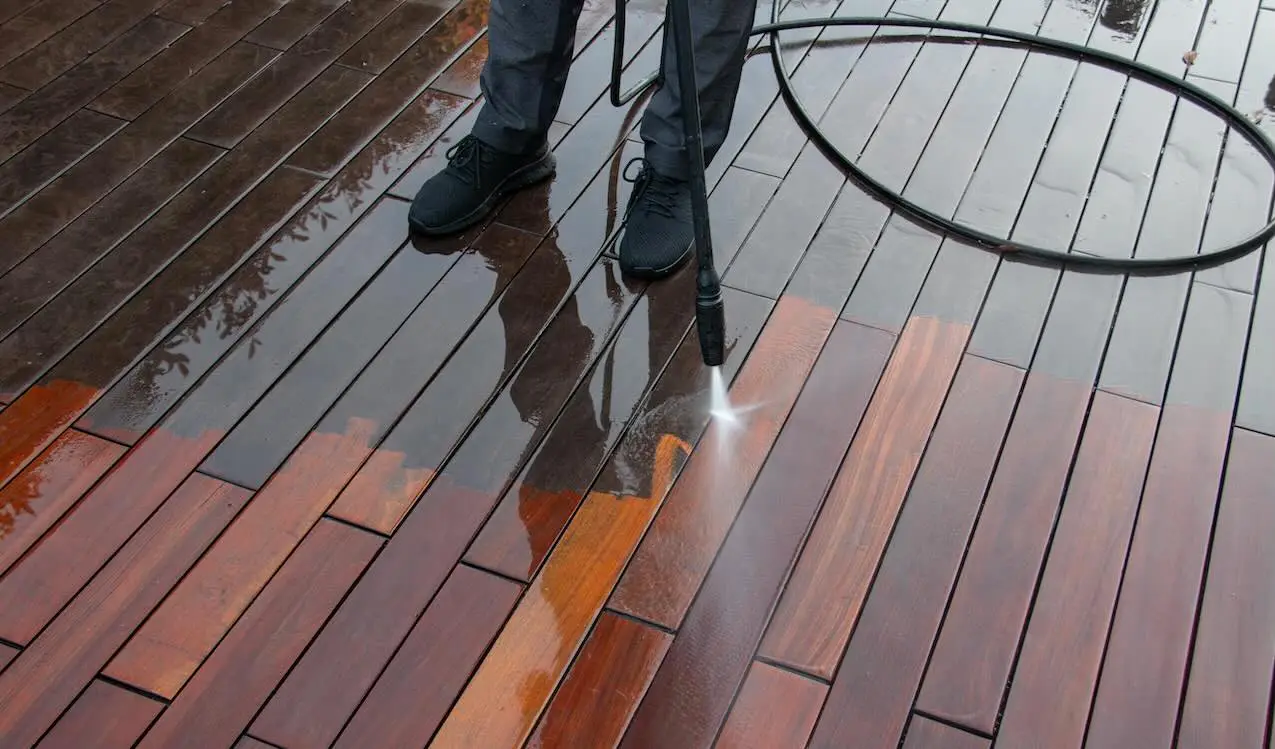 Pressure washing a hardwood deck, showing a sharp line between dull gray boards and clean reddish-brown wood.