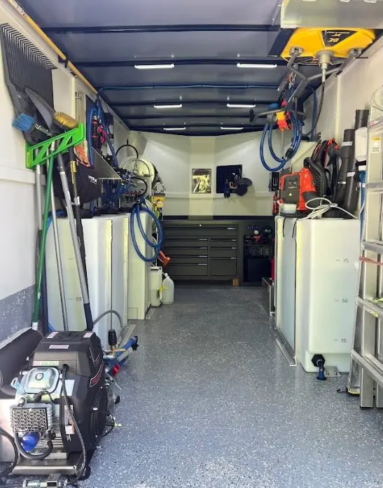 Inside an enclosed work trailer: water tanks, pressure washer engine, hose reels, surface cleaner, ladders and tool chest.