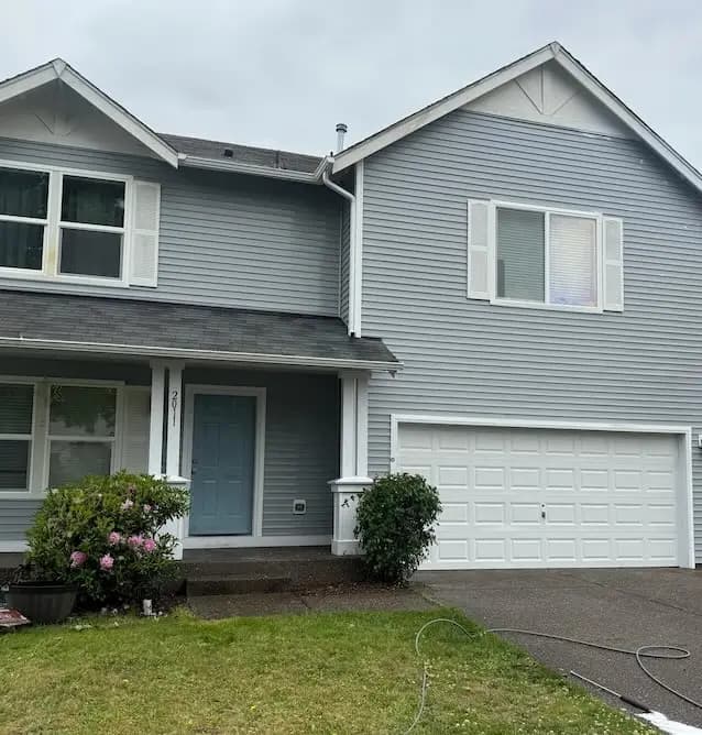 Two-story home with light gray vinyl siding, white trim and a teal front door after house washing.