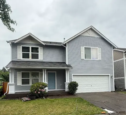 Two-story home with gray vinyl siding, white trim and two-car garage after house washing, hose on the lawn.