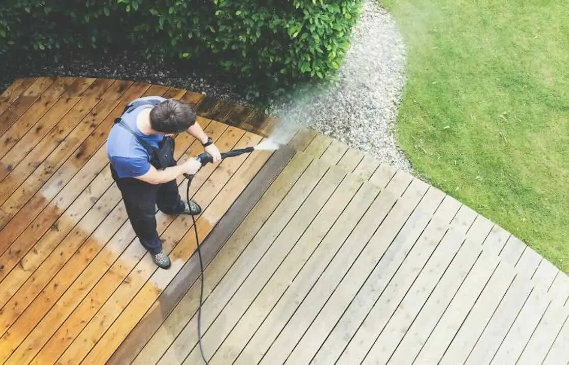 Overhead view of a man pressure washing a curved wood deck, with the cleaned boards clearly lighter than the grimy ones.